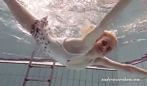 A slender blonde girl swims under water